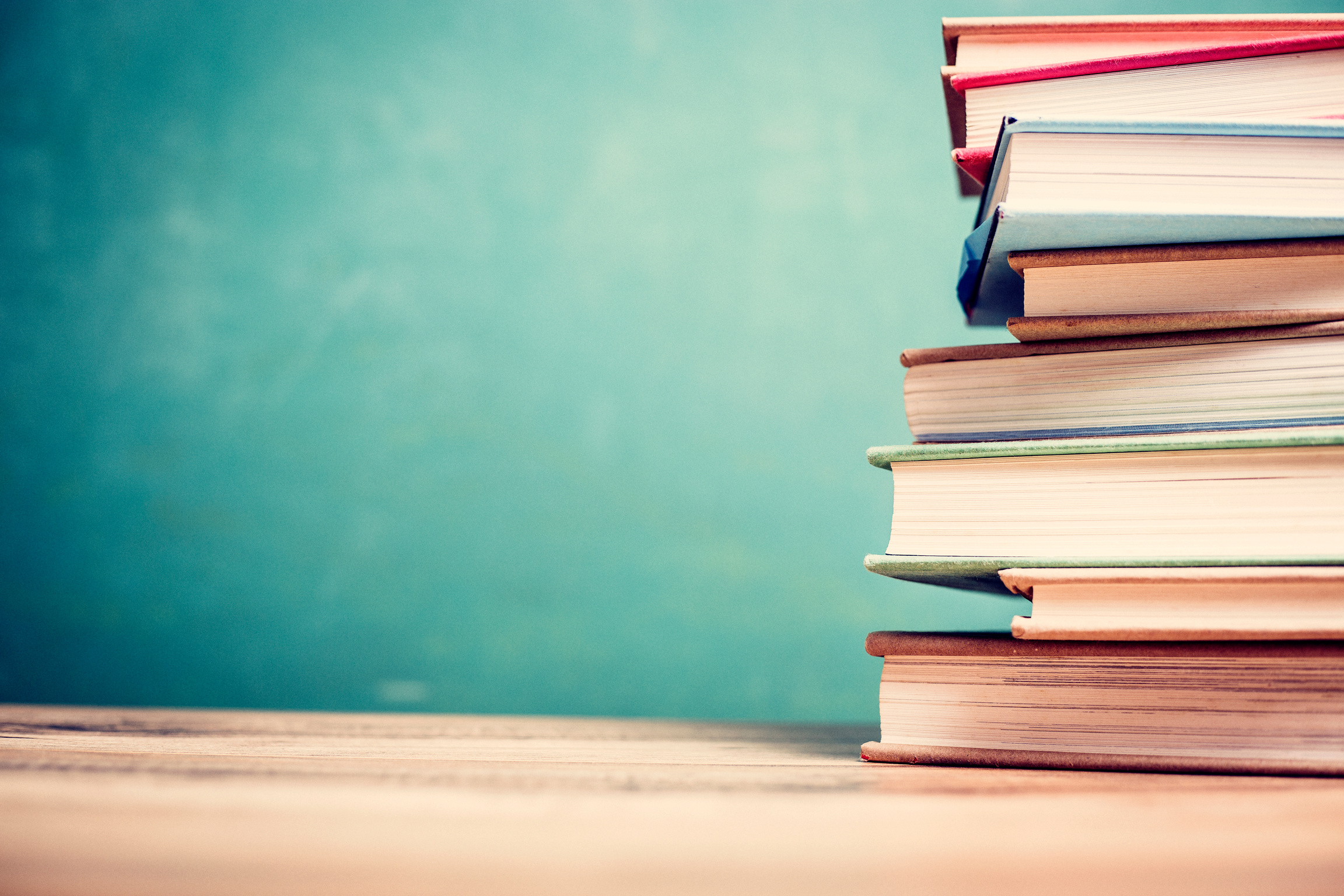 Textbooks on wooden school desk with chalkboard.